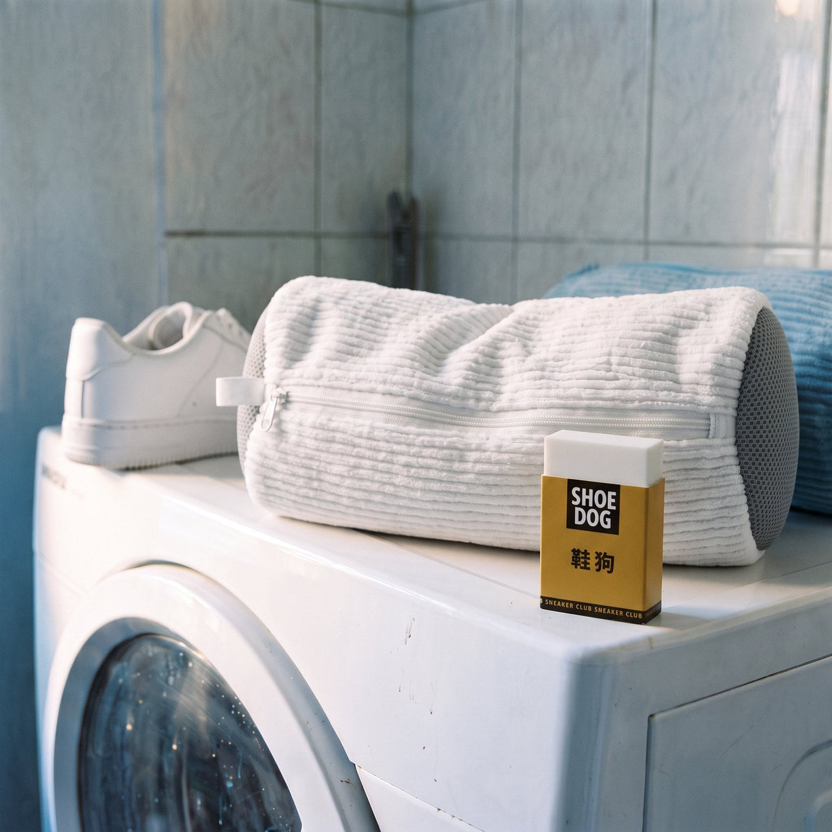 Sac de lavage Kickow fermé sur une machine à laver, une basket propre et la gomme à côté