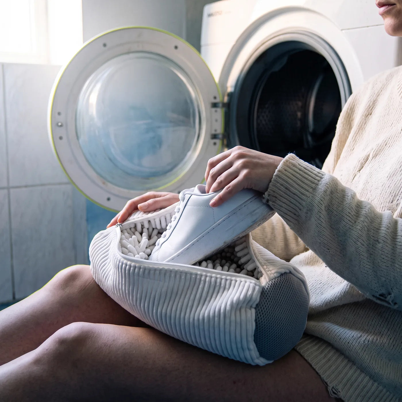 Une chaussure blanche propre sortie du sac posé sur les genoux, devant la machine ouverte
