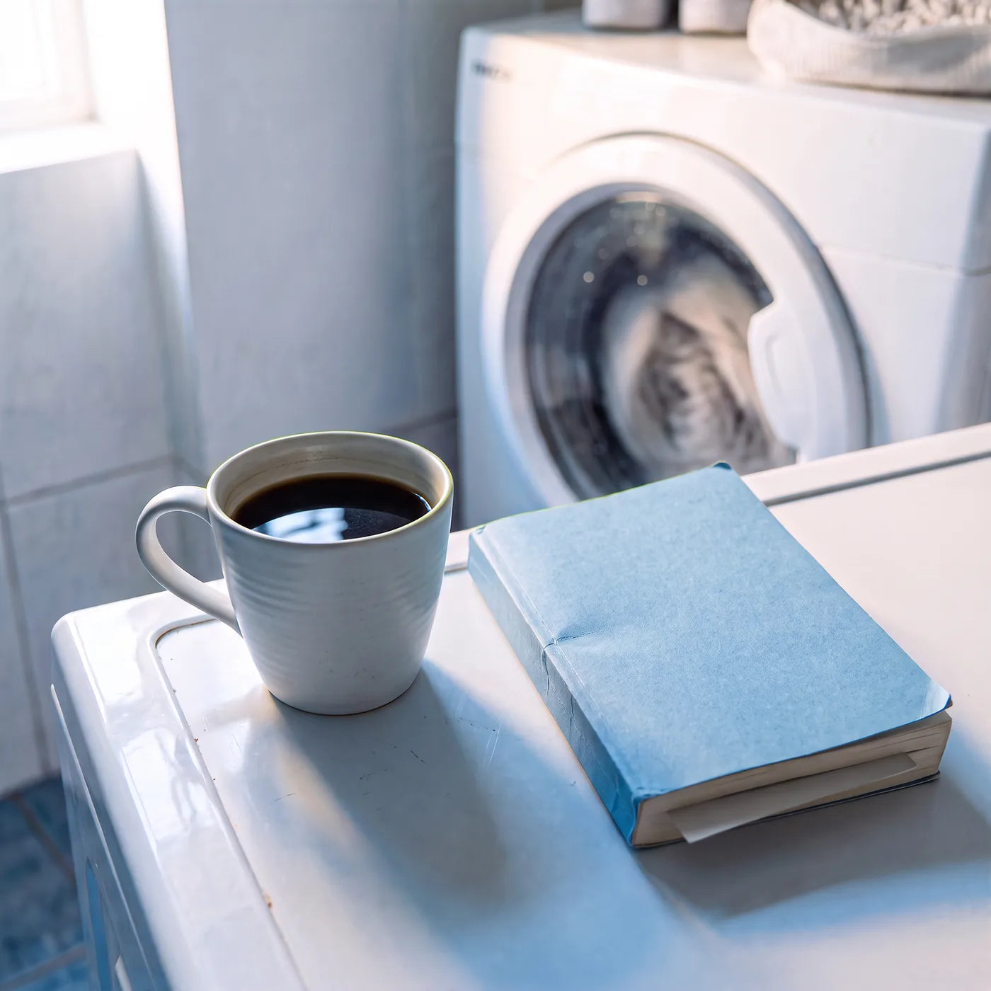 Un café et un livre posés sur la machine pendant que le cycle tourne